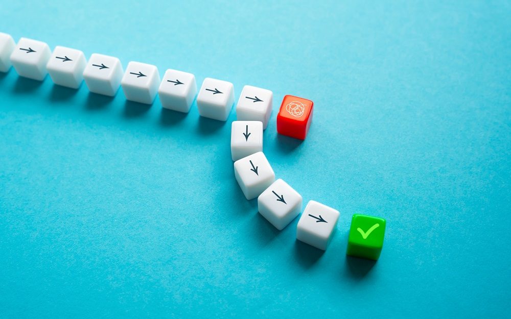 Würfel mit Pfeilen in eine Richtung, die um einen roten Würfel herumgelegt sind und bei einem grünen Würfel mit Häkchen enden