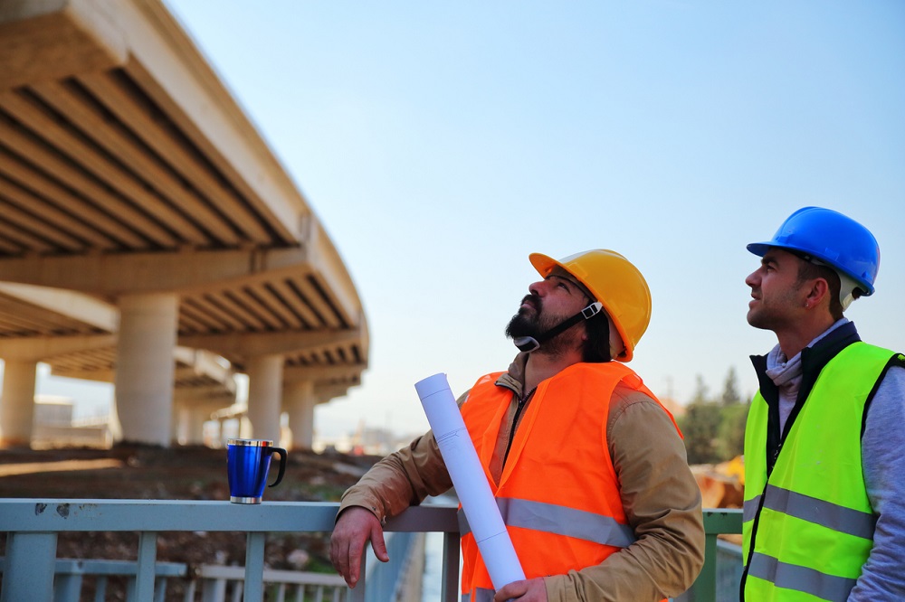 zwei Bauarbeiter blicken nach oben zu einer Brücke im Rohbau