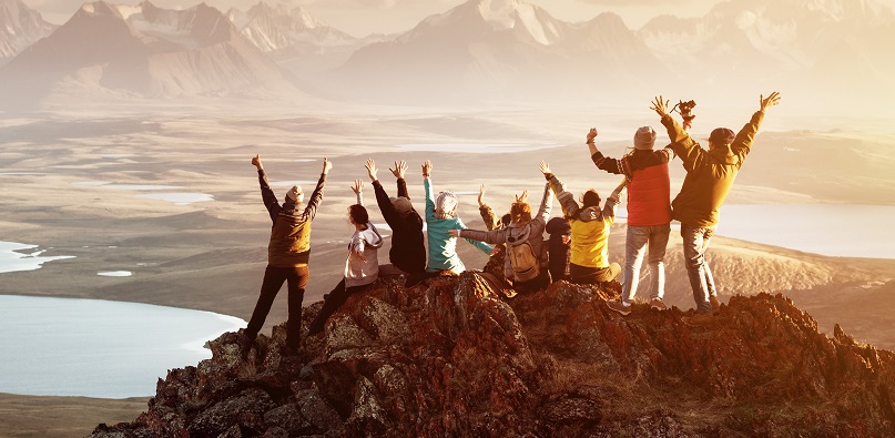 Menschgruppe mit erhobenen Armen von hinten auf einem Gipfel