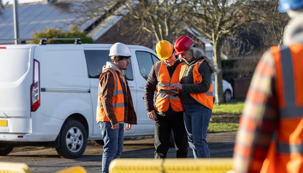 3 Personen mit orangen Warnwesten und Bauhelmen schauen in ein Tablet